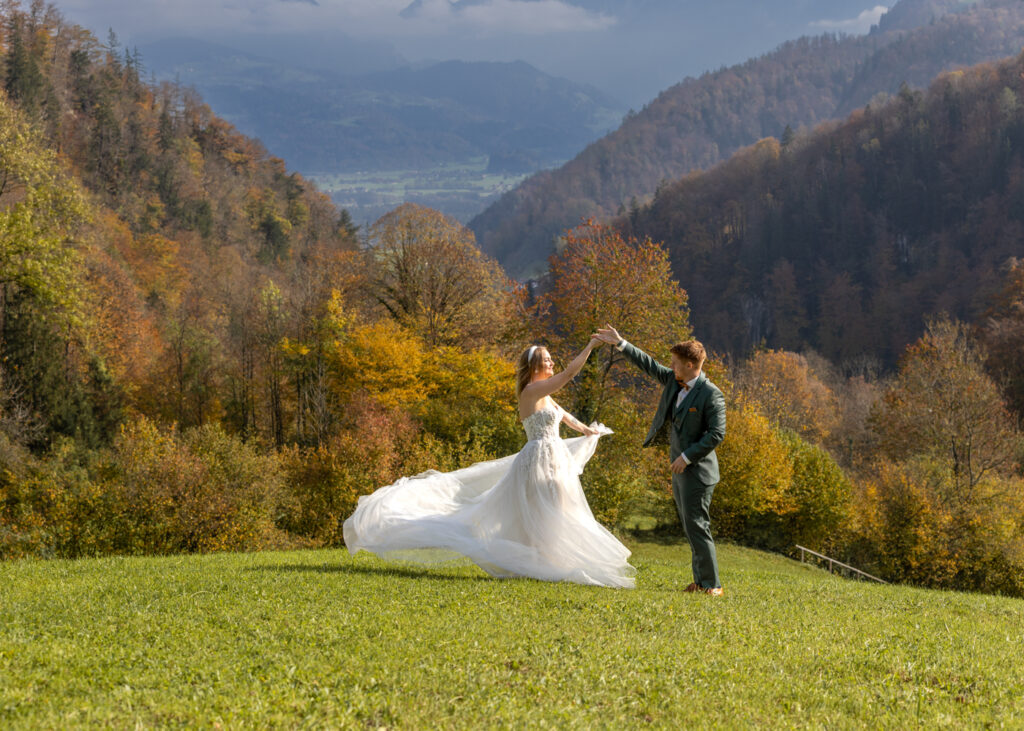 Braut und Bräutigam tanzen auf einer Wiese in Kühschwalb vor herbstlicher Bergkulisse.